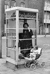361145 Afbeelding van een bellende vrouw in een telefooncel, met een kind in een kinderwagen, in de Bilderdijkstraat te ...
